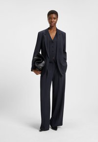 Navy pinstriped blazer with matching wide-leg trousers. The blazer has a tailored fit, notched lapels, and a buttoned vest underneath.