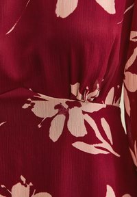 Bordeaux stof met grote lichtroze bloemenprint, met details van een geplooide taille en textuur op het materiaal.