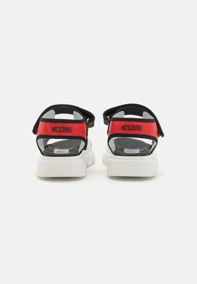 Sandalias negras y rojas con una suela gruesa blanca. Presentan correas ajustables y un contrafuerte de marca. Material suave y diseño abierto.