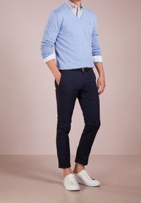 Pull col en V bleu clair, chemise blanche à col sous le pull, associée à un pantalon ajusté bleu marine et des baskets blanches. Aucune motif ou graphisme visible.
