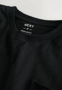 Čierne bavlnené tričko s okrúhlym výstrihom, pravidelným strihom a malou kapsičkou; disponuje jemnou textúrou a jednoduchým dizajnom bez vzorov.