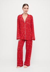 Conjunto de pijama vermelho com mangas longas e calças, apresentando um padrão floral e acabamentos em branco. Feito de um tecido macio e leve.