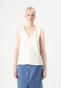 Top sans manches en V crème, avec un tissu doux et texturé et une coupe décontractée. Associé à une jupe en denim bleu clair avec une fente centrale.