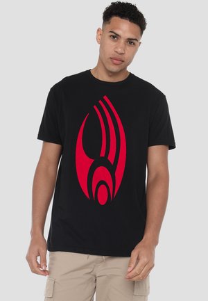 Black cotton t-shirt featuring a large red graphic design resembling flame-like shapes on the front. Crew neck, short sleeves, relaxed fit.