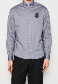 Knappkrage skjorta i lätt blått tyg, med en logotyp på bröstet, långa ärmar med knappmanchetter och en skräddarsydd passform.