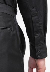 Mustapaita, jossa on terävä kaulus, nappivuori ja sileä kangas, läheltä kuvattuna hihasta ja vyötäröstä.