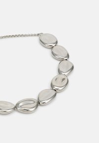 Silberne Halskette mit sieben polierten, unregelmäßig oval geformten glatten Perlen, verbunden durch eine Metallkette auf weißem Hintergrund.