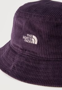 Σκούφος κουβάς από βελούδο κοτλέ σε σκούρο μωβ με λευκό κεντημένο λογότυπο "The North Face" μπροστά.