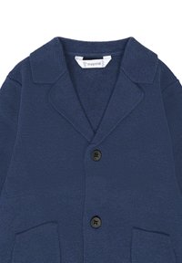 Un cardigan en maille bleu marine avec un col, deux poches avant et trois boutons noirs. La texture est tissée avec un motif légèrement en relief.