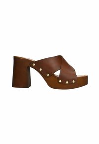 Sandales à talons hauts en cuir marron avec des brides croisées, bout arrondi et clous dorés sur le côté. Talon en bloc épais et base à plateforme.