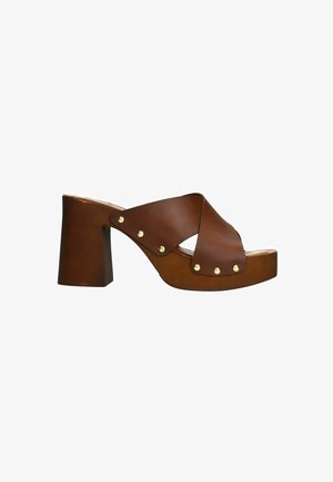 Sandales à talons hauts en cuir marron avec des brides croisées, bout arrondi et clous dorés sur le côté. Talon en bloc épais et base à plateforme.