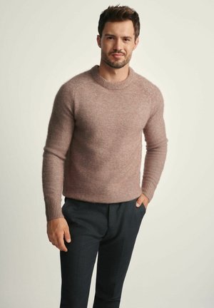 Jasnoróżowy sweter dziewiarski z długimi rękawami i ściągaczami, w połączeniu z ciemnymi spodniami. Sweter ma okrągły dekolt i miękką teksturę.