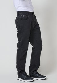 Jeans de mezclilla negros con un corte relajado, diseño de cinco bolsillos y detalles de costura sutiles. Combinados con zapatillas negras con acentos blancos.