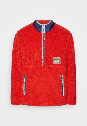 Roter Fleece-Pullover mit marineblauem Halb-Reißverschluss-Kragen, zwei vorderen Reißverschlusstaschen und kleinem Levi's-Patch auf der Brust.