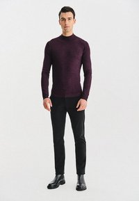 Pulower w głębokim purpurowym kolorze, wykonany z tkanej, fakturowanej tkaniny, z wysokim dekoltem i długimi rękawami. Połączony z czarnymi spodniami typu slim-fit i botkami za kostkę.