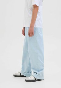 Ljusblå vida jeans tillverkade av denim, med en framficka och vikt upp ärmar. Matchas med svarta och vita sneakers.