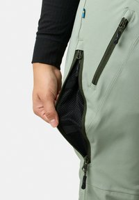 Ljust gröna byxor med en sidoficka med dragkedja. Insidan har ett svart mesh-foder, och det finns en dragflik för enkel åtkomst.