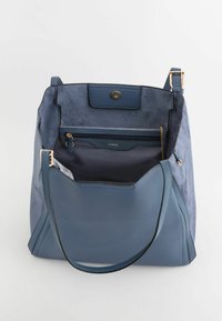 Niebieska torebka o teksturowanym wykończeniu, z zapięciem magnetycznym, wewnętrzną kieszenią na zamek błyskawiczny oraz gładkimi ramiączkami. Wyraźny gradient kolorów od ciemnoniebieskiego do jasnoniebieskiego.