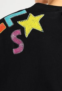 Czarna tkanina z kolorowymi cekinowymi literami i gwiazdką. Kolory to jasnoniebieski, różowy i żółty w różnych rozmiarach i kształtach.