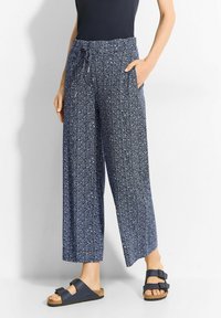 Patterned wide-leg trousers in navy with white floral designs. Lightweight fabric, drawstring waist, and side pockets. Paired with dark sandals.