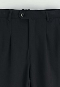 Pantalons noirs sur mesure avec une fermeture à bouton et à zip, ainsi que des passants de ceinture, montrés de la taille à mi-cuisse.