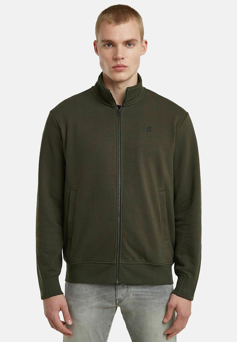 Felpa verde oliva con zip e colletto alto, tasche laterali, polsini a coste e un discreto logo sul petto. Tessuto misto cotone.