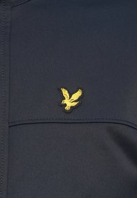 Mornarska pamučna košulja s teksturiranim završetkom, koja sadrži crni i žuti izvezeni logo orla na prsima. Jednostavan dizajn bez dodatnih uzoraka.