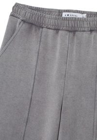 Graue Sweatpants mit elastischem Bund, weichem Material, vorderen Falten, Seitentaschen und sichtbarem Markenlabel am Bund.