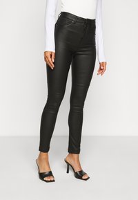 Zwarte kunstleer skinny jeans met een hoge taille, zijzakken en een ritssluiting, gecombineerd met zwarte open teen hoge hakken.