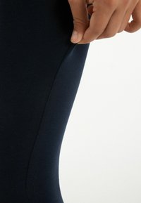 Tyrkysové legíny vyrobené z elastického materiálu, s hladkým povrchem a švem podél strany.