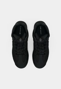 Et par svarte Lacoste-sneakers med tykke såler og detaljerte lisser plassert ved siden av hverandre på en hvit bakgrunn.