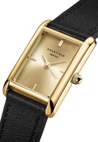 Reloj rectangular dorado con una correa de cuero negro texturizado. La esfera presenta un tono dorado brillante con marcadores de hora simples y una corona en el lateral.