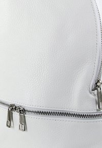 Weiße Leder-Rucksack mit strukturierter Oberfläche, ausgestattet mit einem auffälligen Reißverschluss und silbernem Beschlag sowie einer glatten, abgerundeten Form.