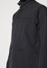 Męska czarna kurtka z wysokim kołnierzem, zamkiem błyskawicznym i dwoma bocznymi kieszeniami. Charakteryzuje się gładką fakturą i minimalistycznym designem.