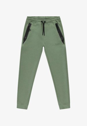 Groene joggingbroek van zacht materiaal, met twee zwarte ritszakken en een elastische tailleband met trekkoord.