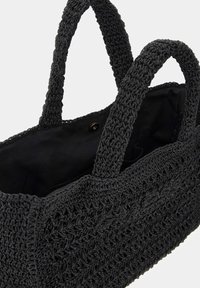 Sac fourre-tout tissé noir avec un design texturé, anses étroites, ouverture en haut et doublure intérieure. Dispose d'une fermeture à bouton et n'a pas de poches extérieures.
