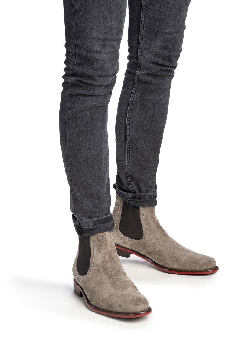Graue Wildleder-Chelsea-Stiefel mit elastischen Seitenpaneelen und einer Sohle mit roten Akzenten, getragen mit engen dunklen Jeans, die ein schlankes, modernes Design zur Schau stellen.