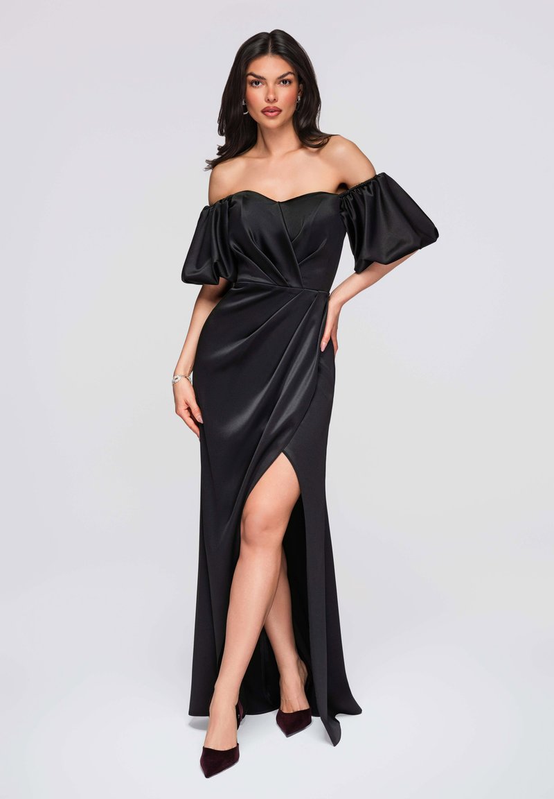 Robe de soirée en satin noir avec manches bouffantes décolletées, corsage ajusté et une fente haute, complétée par des talons bordeaux foncé.