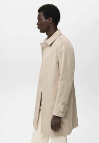 Beige leichter Mantel mit Kragen, seitlichen Schlitzen und knöpfbaren Bündchen. Glatte Textur mit geradem Schnitt.