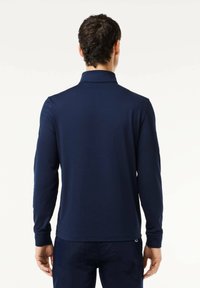 Polo manches longues bleu marine avec col, texture côtelée et surpiqûres contrastées. Tissu doux et ourlet droit.