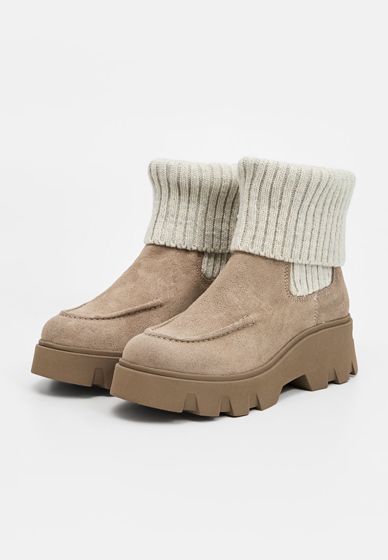 Beige Wildleder Stiefeletten mit einem gerippten Strickbund, ausgestattet mit einer dicken, massiven Sohle und dezenten Nähdetails.