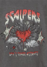 Camiseta gris con el texto en negrita "SCALPERS", gráfico de corazón rojo con un diseño explosivo y acentos de calaveras, texto adicional "NO PERSEQUES, ATRAE."