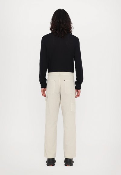 Light beige cargo pants with multiple pockets and a relaxed fit, paired with a black long-sleeve top, viewed from the back.