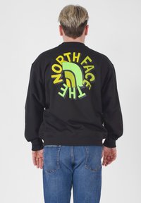 Felpa nera con logo grande e multicolore "North Face" sulla schiena, con accenti verdi, gialli e marroni. Vestibilità comoda e ampia.