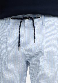 Pantalones cortos de rayas azul claro y blancas con una cintura elástica, cordón negro y extremidades plateadas; tejido suave y texturizado.
