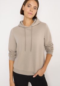 Světle béžová mikina s kapucí a stahovací šňůrkou, nabízející volný střih, žebrované manžety a lem. Hladká textura látky, vhodná pro běžné nošení.