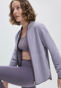 Hellblaue Fleecejacke mit Reißverschluss, rundem Kragen und langen Ärmeln, kombiniert mit einem passenden hellblauen Sport-BH und Leggings.