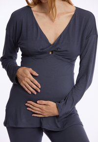 Donkergrijze langemouwen zwangerschapsblouse met een V-hals en gedraaide voorkant, gemaakt van zachte, rekbare stof, gecombineerd met bijpassende onderkleding.