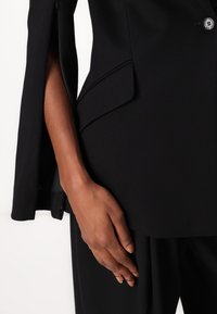 Blazer nero su misura con un design snello, dotato di maniche ventilate, dettagli discreti sulle tasche e chiusura a un solo bottone.