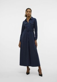 Robe longue bleu marine avec un devant boutonné, un col et une taille ceinturée. Elle possède deux poches poitrine et des manches longues. Texture de tissu lisse.